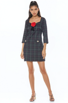 Front view green plaid mini dress, 3/4 sleeve, princess neckline, front pockets with gold trim, rose at neck.