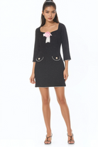 Front view black mini dress, 3/4 sleeve, princess neckline, front pockets with gold trim, rose at neck.