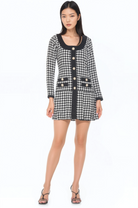 Front view black and white houndstooth mini dress, scoop neck, contrast black detail, gold rim pearl buttons, drop waist and pleated skirt.