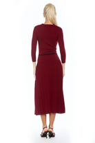 Back view burgundy knit  midi dress with drop waist, contrast black detail, pleated bottom, knit collar and 3/4 sleeves.